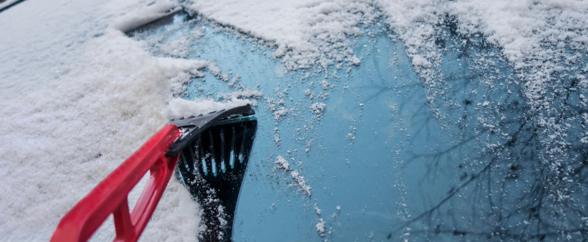 Grattoir qui racle la neige sur le pare-brise d'un véhicule